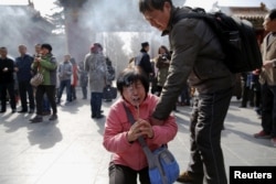 A crying woman falls on her knees as relatives of passengers onboard of Malaysia Airlines flight MH370 which went missing in 2014, burn incense sticks and pray at Lama Temple in Beijing, China, March 8, 2016.