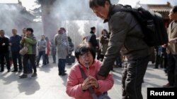 FILE - A crying woman falls on her knees as relatives of passengers onboard of Malaysia Airlines flight MH370 which went missing in 2014, burn incense sticks and pray at Lama Temple in Beijing, China, March 8, 2016. 