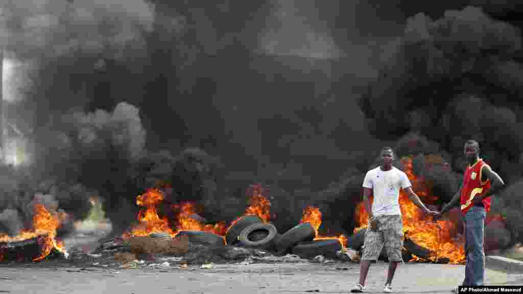 De jeunes gens se tiennent devant une barricade en feu érigée dans le quartier de Koumassi à Abidjan par les partisans du candidat de l'opposition Alassane Ouattara en signe de protestation au président sortant Laurent Gbagbo qui refusent de céder le pouvoir, 6 décembre 2010.