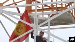 Flag-waving demonstrator climbing a tower at the Kyrgyz Defense Ministry, in Bishkek, 14 Apr 2010