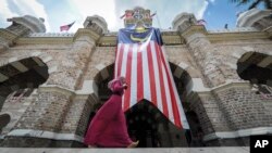 FILE - A Muslim woman walks past a Malaysian flag in front of Sultan Abdul Samad building at Independence Square in Kuala Lumpur, Malaysia.