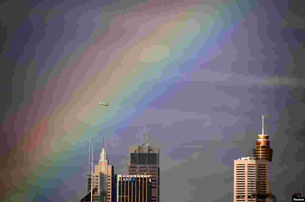 A Qantas Boeing 737 airplane flies through a rainbow above the central business district of Sydney, Australia.