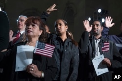 Participants in a naturalization ceremony raise their hands to take the "Oath of Allegiance" at an event attended by President Barack Obama at the National Archives in Washington, Dec. 15, 2015.