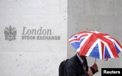 FILE - A worker shelters from the rain as he passes the London Stock Exchange in London.