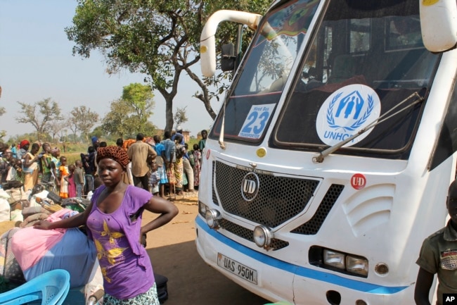 FILE - A women stands in front of a UNHCR passenger bus next to a refugee registration site near Bibi bidi, Uganda.