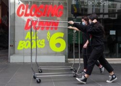 Workers push trolleys past an empty shop in Melbourne’s central business district on August 3, 2020 after the state announced new restrictions as the city battles fresh outbreaks of the COVID-19 coronavirus. - Australia's Victoria state imposed fresh, swe