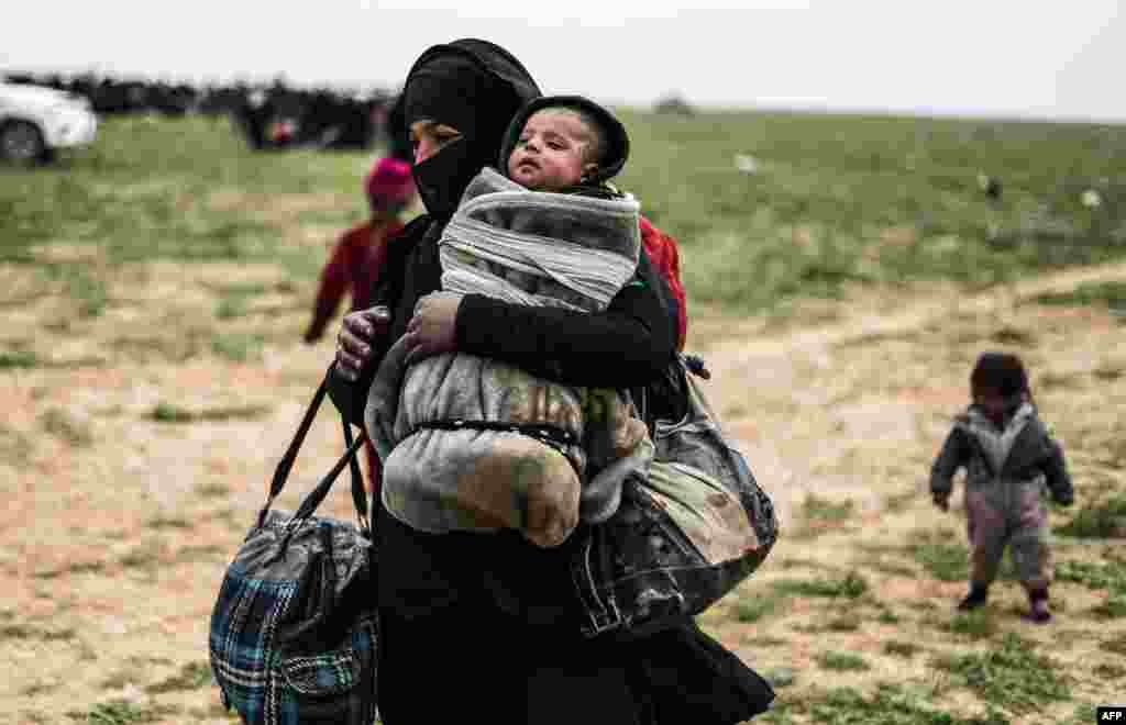 A woman who was evacuated from the Islamic State (IS) group's embattled holdout of Baghuz carries her baby as she walks toward a zone held by the U.S.-backed Syrian Democratic Forces (SDF) during an operation to expel IS jihadists from the area, in the eastern Syrian province of Deir el-Zour, Feb. 26, 2019.