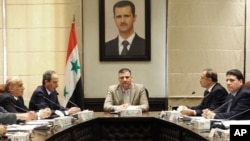 In this undated photo released by the Syrian official news agency SANA on Sunday, Aug. 5, 2012, Syrian Prime Minister Riad Hijab, center, speaks under the portrait of the Syrian President Bashar Assad during a meeting in Damascus, Syria.