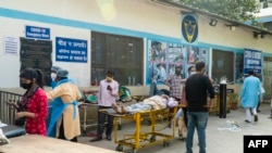 Kerabat menunggu di samping pasien virus corona yang berbaring di tandu di kompleks rumah sakit untuk masuk di New Delhi, 23 April 2021. (Foto: AFP/Maude BRULARD)