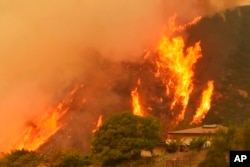FILE - Flames rise behind a home in Santa Barbara, Calif., Dec. 14, 2017.