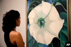 A Tate Modern representative poses for photographs next to "Jimson Weed/White Flower No.1" by American artist Georgia O'Keeffe at a press launch for her retrospective exhibition of over 100 works at the Tate Modern gallery in London, July 4, 2016.