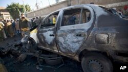 A policeman, background, takes a picture of a damaged car with his cellphone at the scene of a car bombing outside a police academy in Sana'a, Yemen, Jan. 7, 2015. 