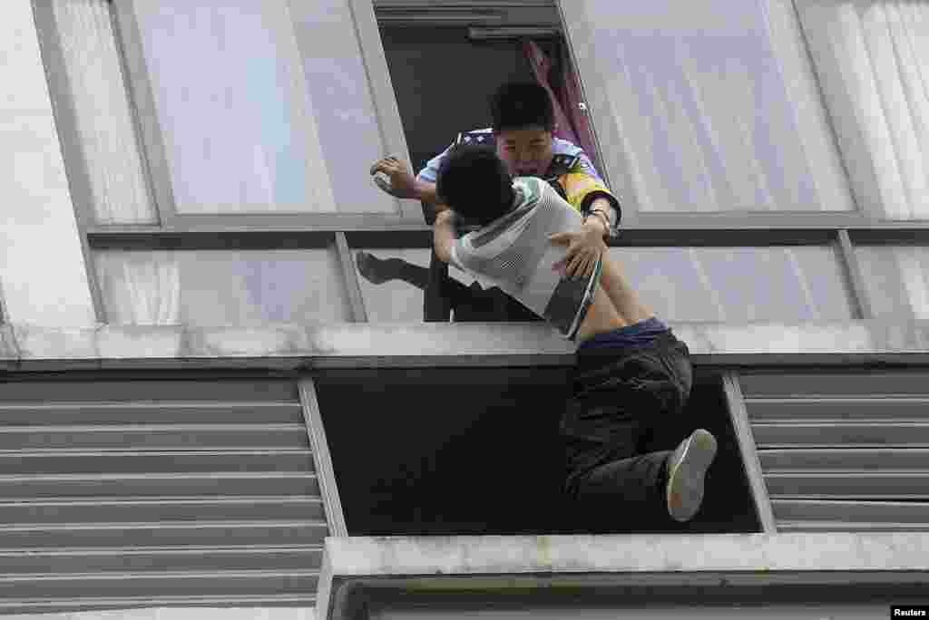 A police officer (top) grabs a man who tries to jump off the seventh floor of a hotel, in Chengdu, Sichuan province, China, May 19, 2014. The 32-year-old man attempted to commit suicide after a failed relationship.