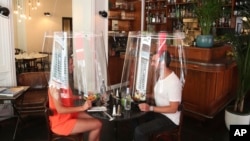 A man and a woman demonstrate dining under a plastic shield Wednesday, May 27, 2020 in a restaurant of Paris. (AP Photo/Thibault Camus)