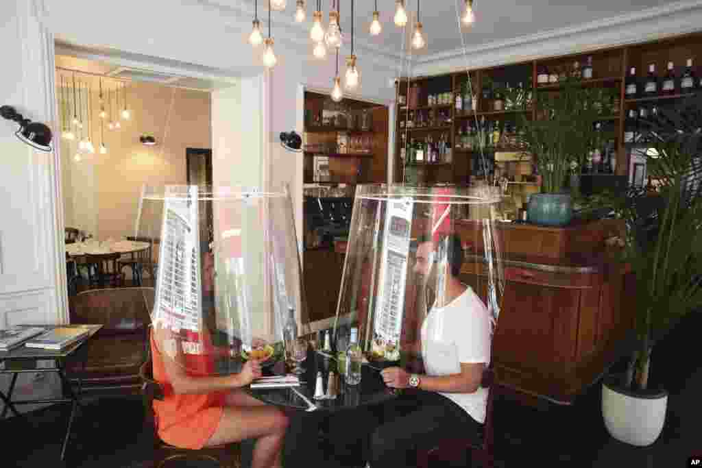 A man and a woman demonstrate dining under a plastic shield Wednesday, May 27, 2020 in a restaurant of Paris. (AP Photo/Thibault Camus)