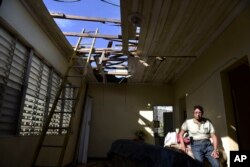 In this Nov. 15, 2017 photo, Edgardo de León sits in his living room with a hole in the ceiling caused by Hurricane Maria, in Cataño, Puerto Rico.