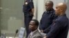 Dominic Ongwen, center, a senior commander in the Lord's Resistance Army, whose fugitive leader Kony is one of the world's most-wanted war crimes suspects, sits in the court room of the International Court in The Hague, Jan. 21, 2016.