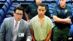 Zachary Cruz, center, the brother of the Florida school shooting suspect, is displayed in a monitor via closed circuit television from the main jail as he as he makes his first appearance on charges of trespassing on the grounds of Marjory Stoneman Douglas High School, March 20, 2018, at the Broward County Courthouse in Fort Lauderdale, Fla.