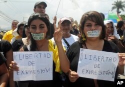 FILE - Journalists and protesters march with their mouths taped shut that read in Spanish "If I speak I die" and hold signs that read "Freedom of expression!" as they protest violence against members of the media in the capital city of Tegucigalpa, Honduras. A new book highlights some of the abuses against female reporters.