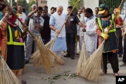 FILE - Indian Prime Minister Narendra Modi, center, sweeps an a road with a broom along with civic workers in New Delhi, Oct. 2, 2014.