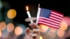 A mourner holds up an American flag and a candle during a vigil for a fatal shooting at an Orlando nightclub, June 12, 2016, in Atlanta.