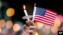 Seorang pelayat membawa bendera Amerika dan menyalakan lilin dalam doa bersama untuk para korban penembakan di klub malam di Orlando, Florida (12/6).