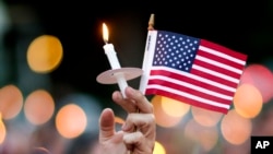 A mourner holds up an American flag and a candle during a vigil for a fatal shooting at an Orlando nightclub, June 12, 2016, in Atlanta.