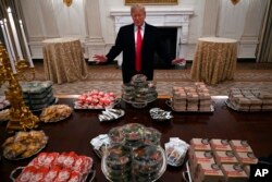 In this Jan. 14, 2019 photo, President Donald Trump talks to the media about the table full of fast food in the State Dining Room of the White House in Washington, for the reception for the Clemson Tigers.