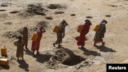 FILE - Women carry jerry cans of water from shallow wells dug from the sand along the Shabelle River bed, which is dry because of drought in Somalia's Shabelle region, March 19, 2016.