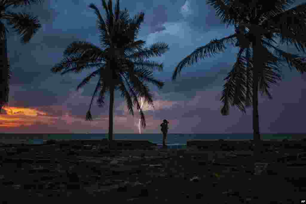 A photojournalist is silhouetted by the sunset as lightning strikes at a resort affected by the tsunami, in Carita, Indonesia.