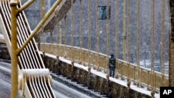 A man walks across the Rachel Carson bridge over the Allegheny River toward downtown Pittsburgh as snow falls during the evening rush hour, Jan. 20, 2016. 