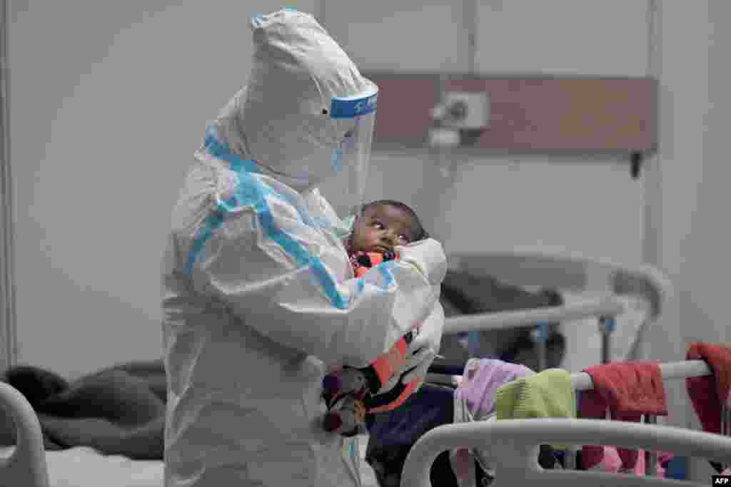 A health worker wearing a personal protective equipment suit holds a child infected with COVID-19 inside a ward at the Commonwealth Games village sports complex, temporarily converted into a coronavirus care center, in New Delhi.