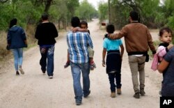 FILE - Migrant families walk from the Rio Grande, the river separating the U.S. and Mexico in Texas, near McAllen, Texas, right before being apprehended by Border Patrol, March 14, 2019.