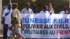 A soldier walks past Malians protesting the junta's arrest of several prominent figures in April