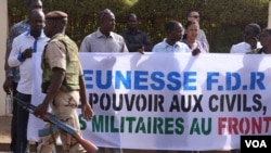 A soldier walks past Malians protesting the junta's arrest of several prominent figures in April