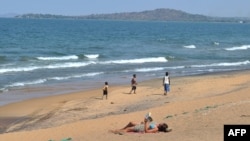 A woman reads a book as young boys pass by on the Saga beach at Lake Malawi, July 17, 2011. 