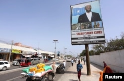 People walk along a street with the campaign billboard of Somalia's Presidential candidate Sharif Sheikh Ahmed in Somalia's capital Mogadishu, Feb. 6, 2017.