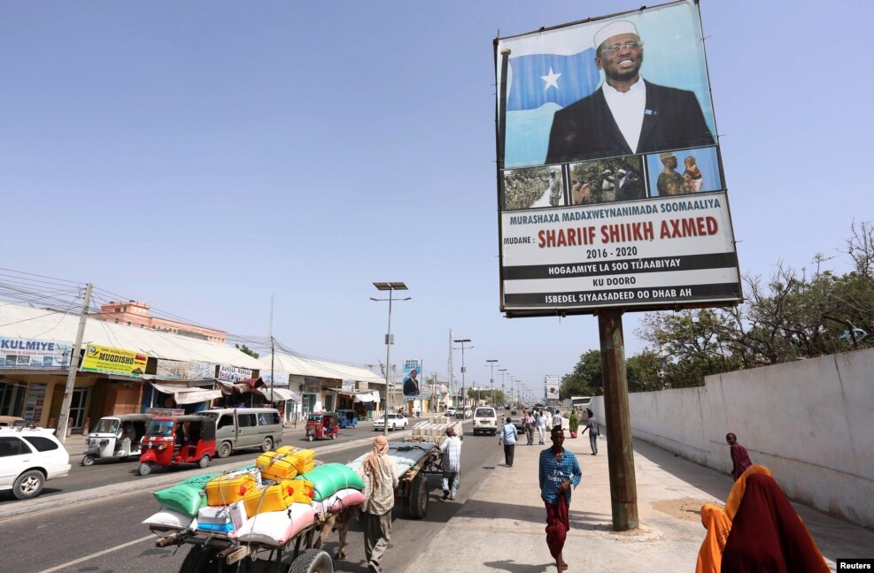 People walk along a street with the campaign billboard of Somalia's Presidential candidate Sharif Sheikh Ahmed in Somalia's capital Mogadishu, Feb. 6, 2017.