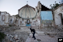 FILE - A man sweeps an exposed tiled area of the earthquake-damaged Santa Ana Catholic church, where he now lives, in Port-au-Prince, Haiti, Jan. 12, 2013.