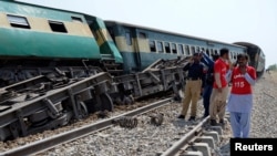 A police officer and rescue workers stand near to a derailed passenger train, after a bomb went off on track in Naseerabad, Pakistan, March 17, 2019. 