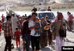 FILE - Displaced people from the minority Yazidi sect, fleeing violence in the Iraqi town of Sinjar, re-enter Iraq from Syria at the Iraqi-Syrian border crossing in Fishkhabour, Dohuk province, Aug. 10, 2014.