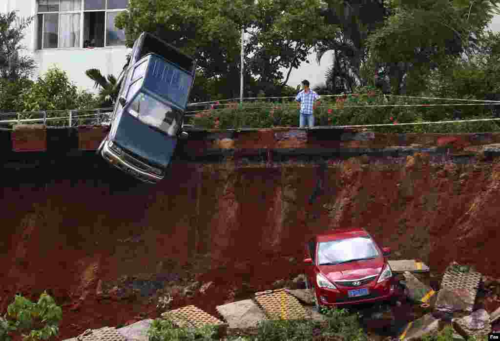 A man looks on as cars are seen stuck in a sinkhole in a parking area after heavy rainfall in Haikou, Hainan province, China.