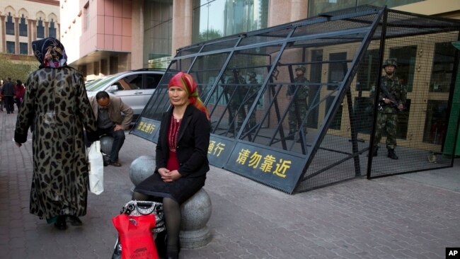 2014年5月1日，一名维吾尔族妇女在一个由中国武警重兵把守的大楼入口处休息。