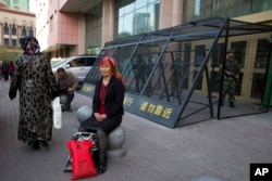 FILE - An Uighur woman rests near a cage protecting heavily armed Chinese paramilitary policemen on duty in Urumqi in China's northwestern region of Xinjiang, May 1, 2014.