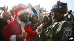 Một người biểu tình Palestine ăn mặc như ông già Noel đưa kẹo cho một cảnh sát Israel ở thành phố Bethlehem ở Bờ Tây hôm 18/12.