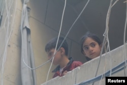 Children look out from a balcony at a site hit by airstrikes in the rebel-held area of Aleppo's Bustan al-Qasr, Syria, April 29, 2016.