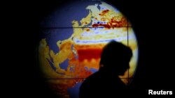 FILE - A woman walks past a map showing the elevation of the sea in the last 22 years during the World Climate Change Conference 2015 (COP21) at Le Bourget, near Paris, France, Dec. 11, 2015. 