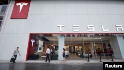 FILE - People walk past a showroom outside Tesla China headquarters at China Central Mall in Beijing, China, July 11, 2018.