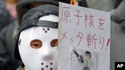 A protester wearing a mask holds a sign at a rally, in front of the headquarters of Tokyo Electric Power Company [TEPCO], aimed at criticizing TEPCO and demanding the abolition of nuclear power, in Tokyo, March 3, 2012. 