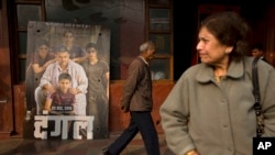 An elderly man walks past a poster of Bollywood movie 'Dangal,' a 2016 Bollywood biopic on an Indian wrestling coach and his two professional wrestler daughters, outside a theater in New Delhi, India.